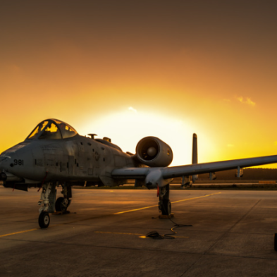 Military plane on the runway backlit by the sunset.