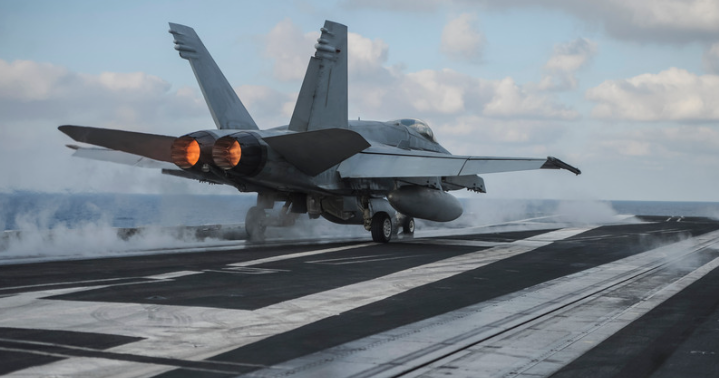 Military jet taking off of an aircraft carrier at sea.